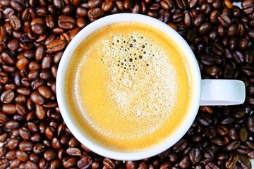 Top view white coffee cup filled with hot coffee surrounded by roasted coffee beans as background.