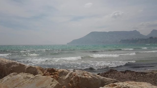 Sunny day at Costa Blanca with mediterranean sea waves and mountain hills at the background