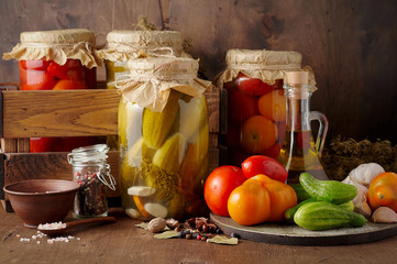 Homemade pickled tomato and cucumber in glass jars on an wooden rustic background