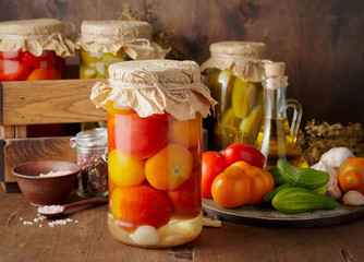 Homemade pickled tomato and cucumber in glass jars on an wooden rustic background