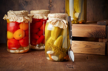Homemade pickled tomato and cucumber in glass jars in wooden rustic box
