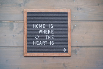Grey lettering Board with felt coating in wooden frame with English text home is where the heart is on the wall of wooden house