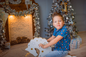 Boy rides a toy rocking horse, Christmas concept, fireplace and a toy tree in the background