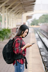 Fototapeta premium Young beautiful female travel photographer enjoys taking photo during her trip at railway station. Asian woman travel with camera having fun making pictures while waiting for train.