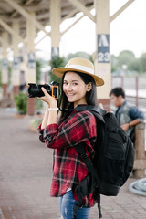 Fototapeta na wymiar Young beautiful female travel photographer enjoys taking photo during her trip at railway station. Asian woman travel with camera having fun making pictures while waiting for train.
