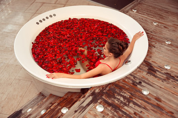 Spa Relax. Beautiful girl in jacuzzi. Bikini Woman lying in round bath with red rose petals. Health And Beauty. Sexy Girl in red swimwear Bathing With red lips. Treatment, Aromatherapy Skin Bodycare.