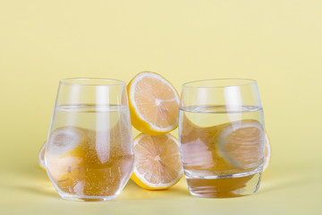 Half lemons and water glasses on yellow background