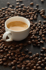 White cup with espresso on dark surface with coffee beans