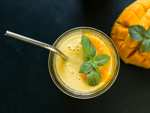 top view on mango smoothie / mango lassi in vintage glass cups on a dark surface with metal straws. with mint leaves and a slice of ripe and juicy mango
