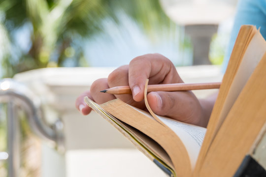 Student reading a old book. Sitting at terrace home in autumn forest, holds book in hands with pencils. Reading is complex cognitive process of decoding symbols to derive meaning.