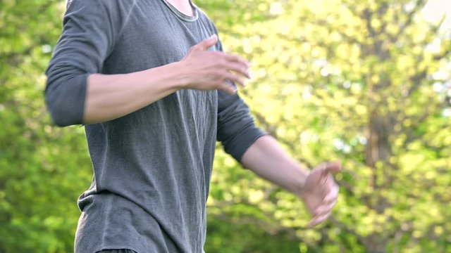 An average plan a young man in Indian clothes and pants Aladdin practices qigong while doing exercises while working with qi energy outdoors in summer next to an old hut