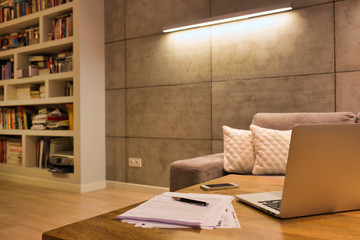 Laptop and documents on table against illuminated wall in apartment