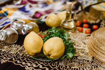 Fototapeta na wymiar Quince fruits on a table decorated with oriental fabrics with ornaments and gold accents. The concept of oriental cuisine. Quince fruit, tomatoes and herbs are on the table.
