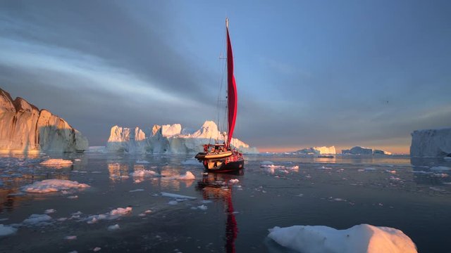 Sailboat moving in Disko Bay by icebergs