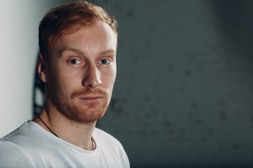 Portrait of a young blond man. He is wearing a white T-shirt. He is tired and thoughtful.