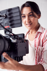 Female Videographer With Video Camera Filming Movie In White Studio