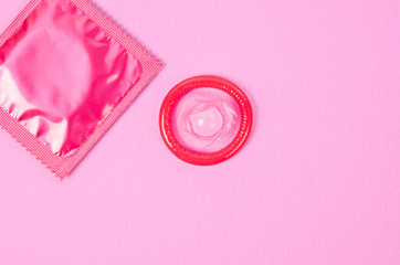 Pink opened condom and condom in pack.