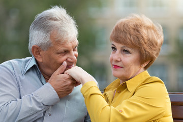 An old man kisses the hand of his wife Lovers aged people are sitting on a bench a man kisses a woman hand