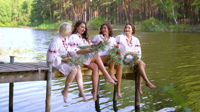 Pretty women in ethnic dresses with floral circlets sitting on wooden bridge