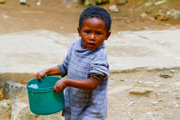 Poor malagasy boy carrying plastic bucket - poverty