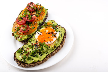 Sandwiches with avocado guacomole, egg and tomatoes, green leek and sesame seeds. Healthy breakfast or snack on a white background.