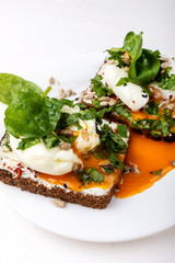 Sandwiches with poached eggs, cheese, spinach leaves, sesame seeds and seeds. Healthy breakfast or snack on the white background. Close-up.