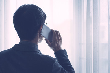 Back side of man using mobile phone with window light