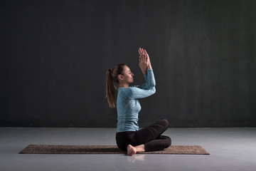 Young woman sitting in Gomukhasana, Cowface pose variation. Studio full length shot