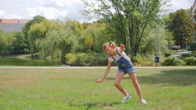 Little cute girl on park grass makes sport acrobatic rotation on hands having fun outdoors