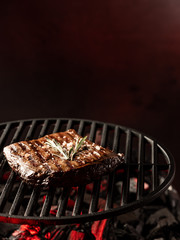 Cooking beef meat steak on hot grill barbecue with fire flams and smoke on black background.