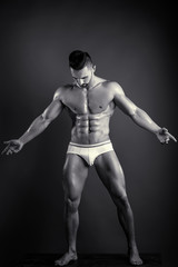 Man shows his muscules. Handsome guy in white underwear shows his well trained body. Black and white studio photo of young male model. Man looking on his abs.
