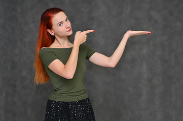 Portrait of a pretty red-haired girl, a happy young woman in a green T-shirt and black skirt on a gray background in the studio. Smiling, showing different emotions.