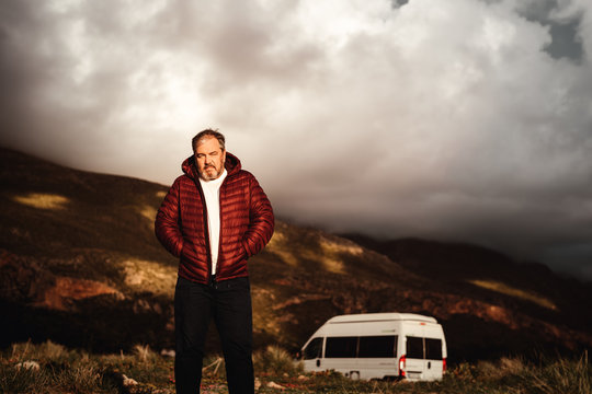 Mann mit wei&szlig;em Tshirt und weinroter Jacke steht in Landschaft mit Van im Hintergrund