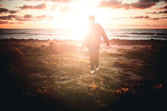 Mann wandert am strand mit Blumen in der Hand bei sonnenuntergang