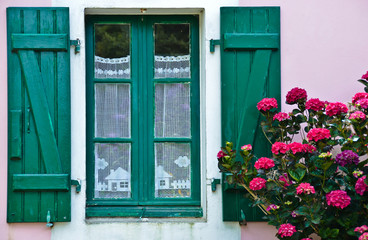Obraz na płótnie Canvas Sonniger Blick auf ein Fenster mit grünen Fensterläden, in dem eine gehäkelte, weiße Gardine hängt.