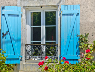 Fototapeta na wymiar Sonniger Blick auf ein Fenster mit leuchtend blauen Fensterläden vor dem ein verziertes Metallgitter ist