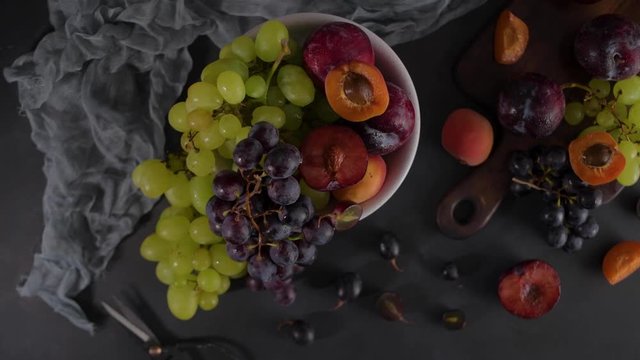Fruits Still life with fruit on white ceramic bowl. Concrete wall. Dramatic light. Grapes, apricots and plums.