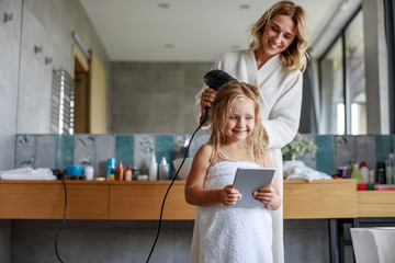 Smiling cute girl is holding tablet in bathroom