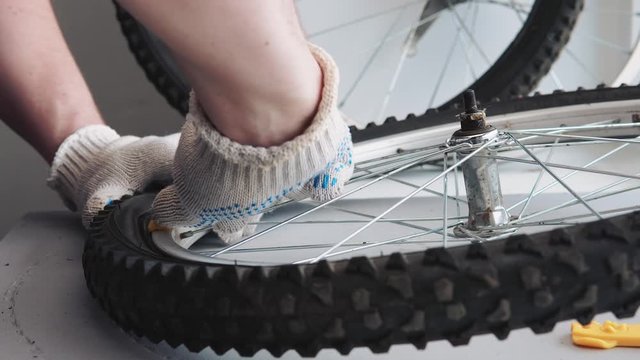 A male mechanic is repairing a bicycle wheel. Closeup of a hand in gloves disassemble a bicycle wheel tire using shoulder blades.