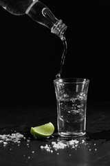 Pouring vodka into the shot glass on a black background with a blank space for a text, Russian vodka with salt and lemon