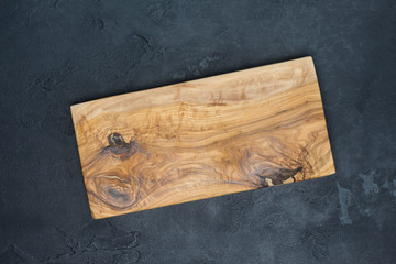 Wooden cutting board from olive tree on dark concrete background. Cooking, recipe concept. Top view, flat lay, mock up, copy space