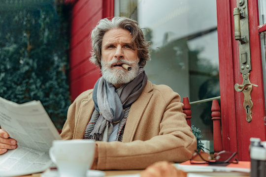 Handsome Senior Man Smoking Cigar At Outdoor Cafe