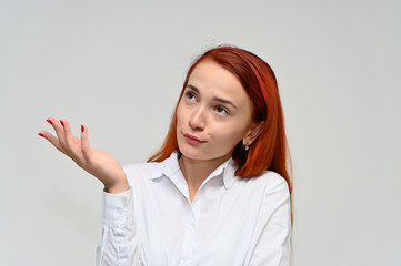 Close-up Portrait of a pretty red-haired girl, a happy young woman manager in a white shirt on a white background in studio. Smiling, showing different emotions.