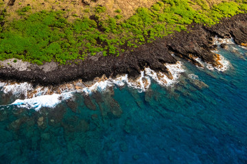 Aerial view of ocean with dark lava rock and bright green vegetation near Keauhou Point Hawaii