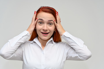 Close-up Portrait of a pretty red-haired girl, a happy young woman manager in a white shirt on a white background in studio. Smiling, showing different emotions.