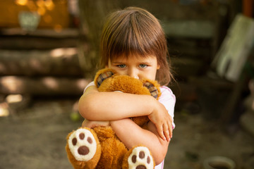 Portrait of adorable toddler girl hugging a teddy bear outdoors, sad face expression, day