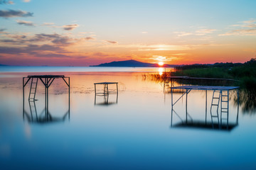 sunrise with sun peaking out of the mountain at lake balaton hungery, with nice reflections in the water fonyód district hungary summer vacation travel relax - obrazy, fototapety, plakaty