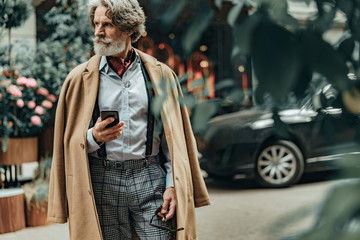 Elegant senior man with smartphone standing on the street