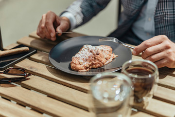 Gentleman with knife and fork eating pie at outdoor cafe