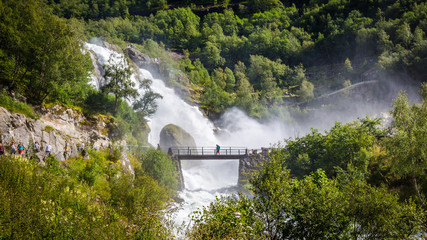 Fototapeta na wymiar Bridge and waterfall with melting water of the Briksdal glacier in Norway, arm of Jostedalsbreen glacier in Oldedalen valley in Norway, Scandinavia.